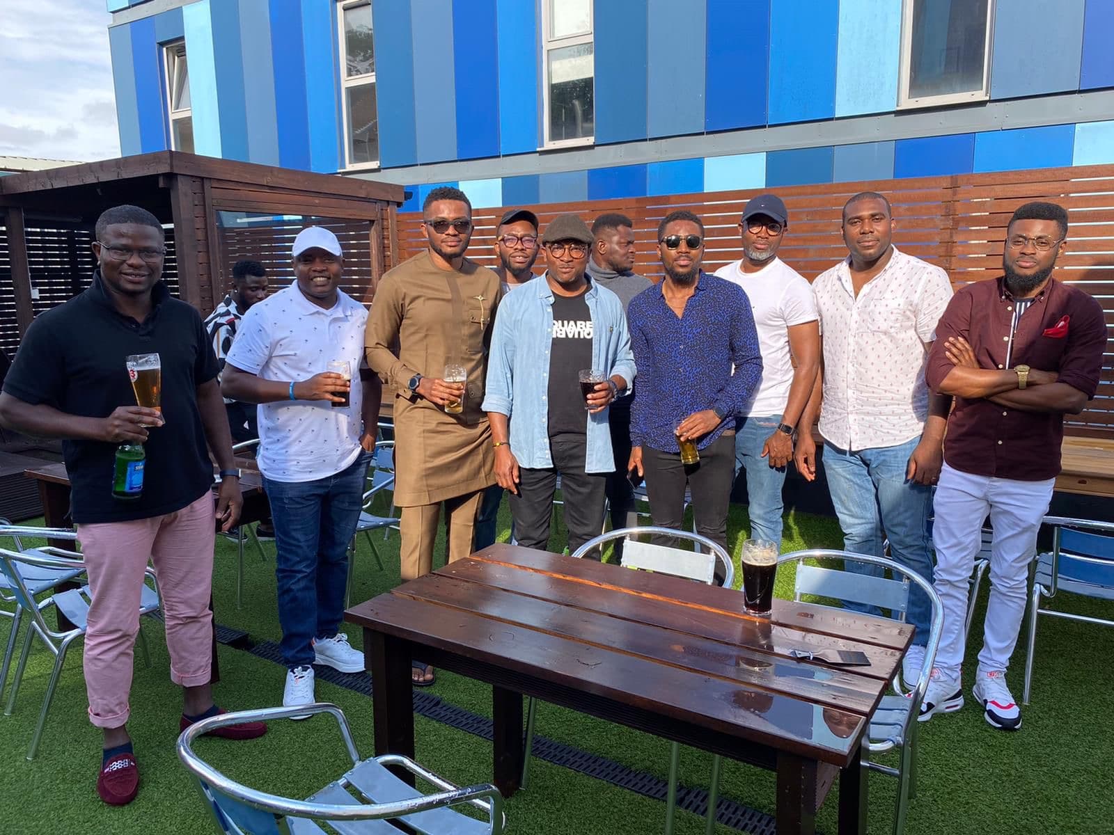 Brothers gathered on a sunny terrace, drinks in hand, after a community hangout.