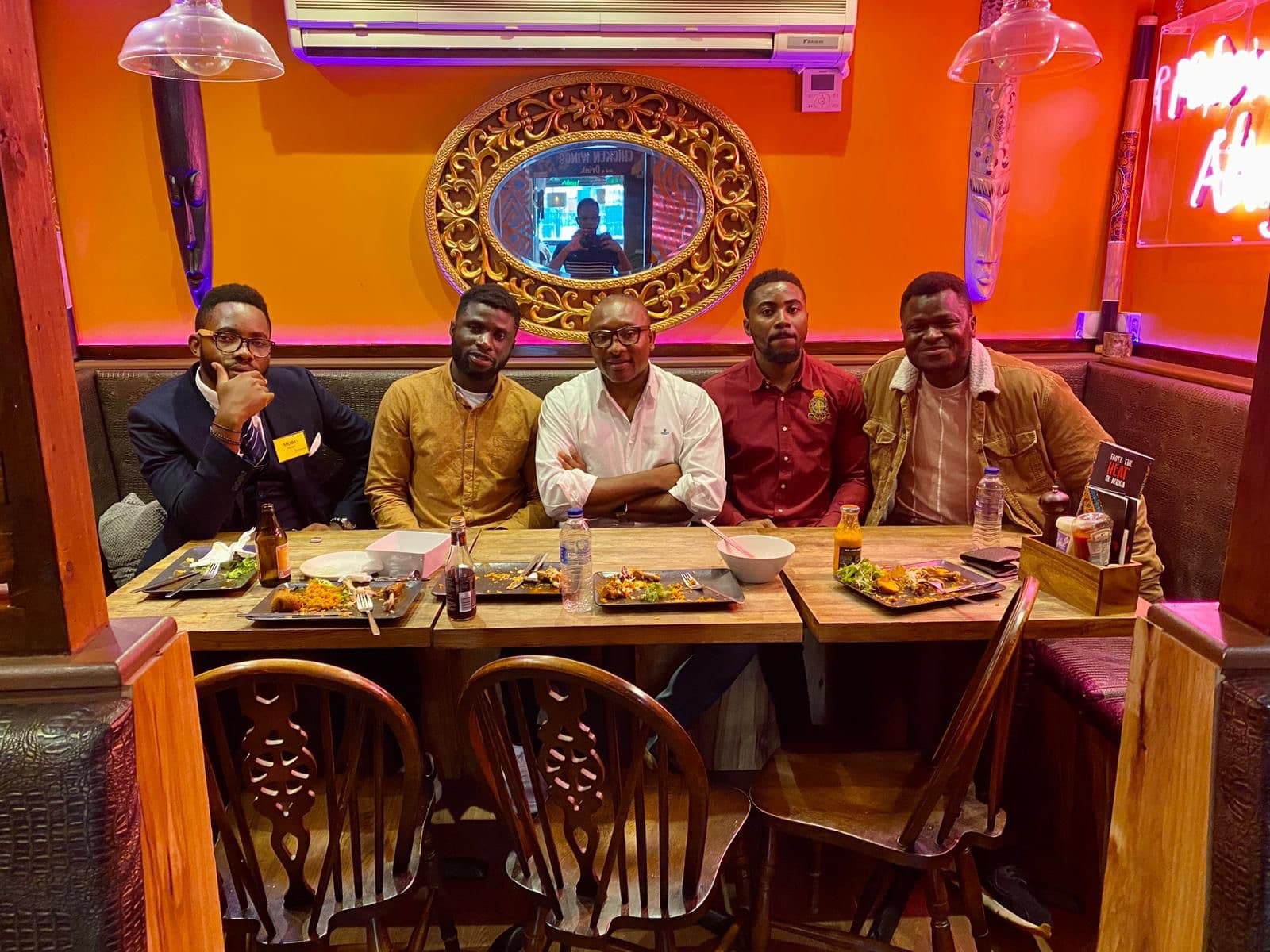 Five men sharing a meal in a warmly lit restaurant.